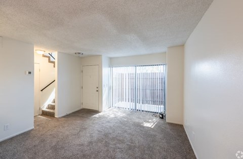 A room with a carpeted floor, a sliding glass door, and a staircase.