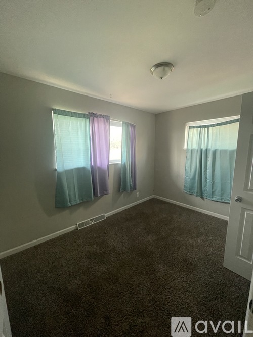 A room with a carpeted floor and two windows with curtains.