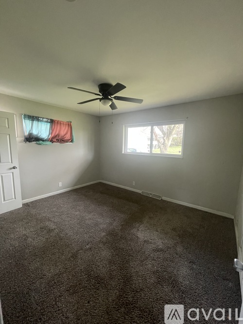 A room with a ceiling fan and a window with a red curtain.