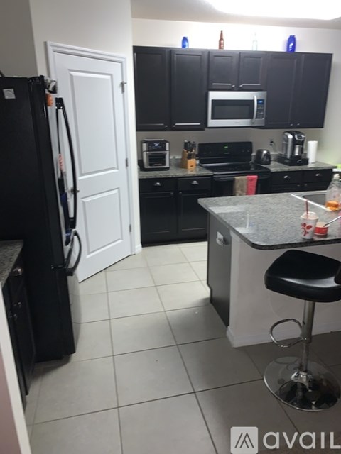 A black refrigerator is in a kitchen with black cabinets and a white door.