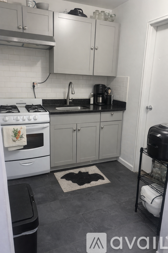 A kitchen with white appliances and a black trash can.