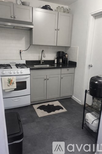 A kitchen with white appliances and a black trash can.