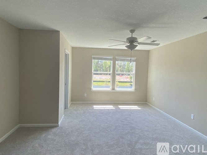 A room with a ceiling fan and a window with a view of trees and a parking lot.