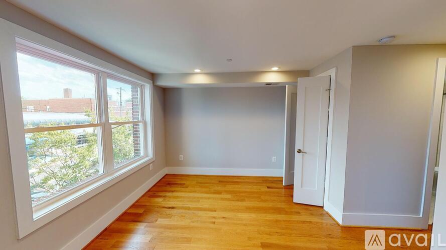 A room with wooden floors and white walls, with a window showing a view of a building and trees.