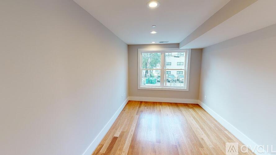 A room with wooden flooring and a window showing a view of trees and buildings outside.