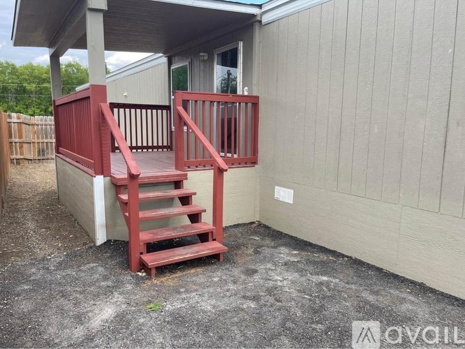 A red wooden staircase with a railing is in front of a grey building.