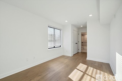 A spacious room with wooden floors and a window with blinds.
