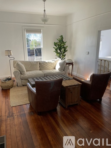 A living room with a white couch, a brown chair, and a wooden floor.
