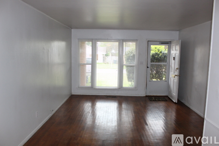 A room with wooden floors and white walls, with a door and windows.