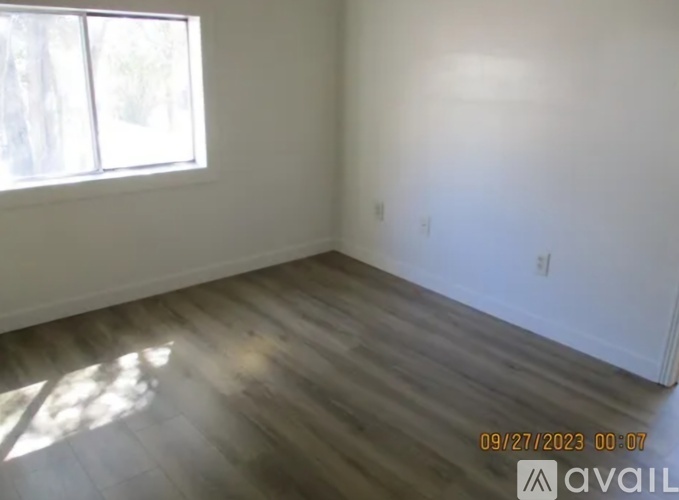 A room with wooden flooring and a window letting in sunlight.