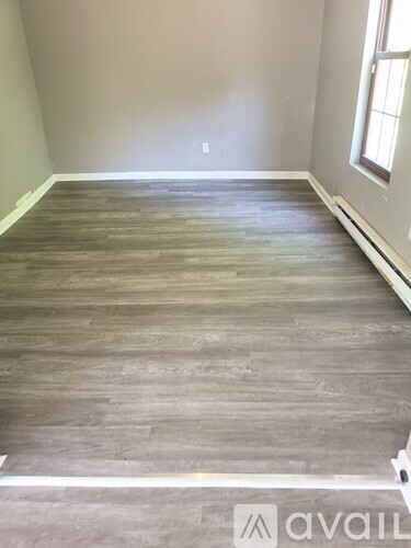 A room with wooden flooring and a window on the right side.