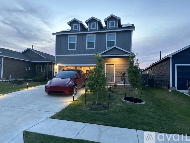 A red car is parked in front of a grey house.