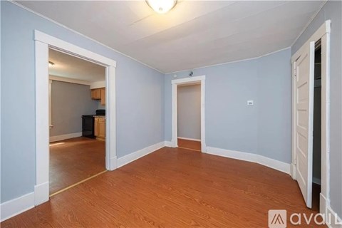 A room with wooden floors and white walls, with a doorway leading to another room.