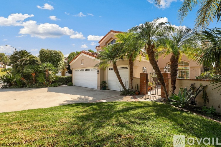 A house with a white garage door is surrounded by greenery and palm trees.