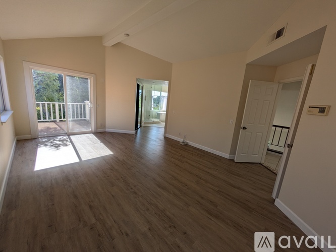 A spacious room with wooden flooring and a balcony with a view of trees.