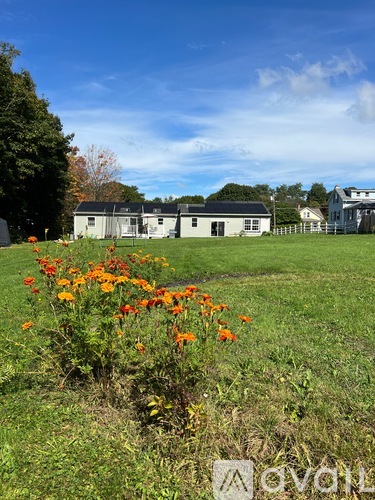 A field with flowers in the foreground and a white building in the background.