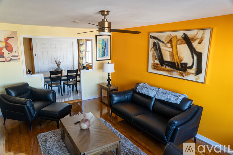 A living room with a black leather couch and a painting on the wall.