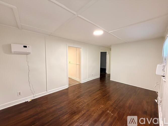 A room with wooden floors and white walls, with a door on the right and a window on the left.