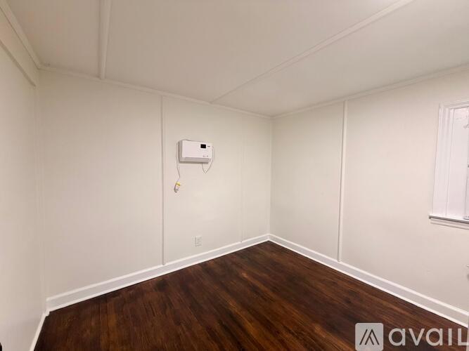 A room with a white ceiling, wooden floor, and a window with a white frame.