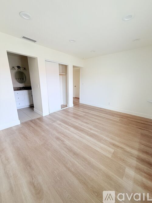 A room with wooden flooring and a white wall with a doorway leading to another room.