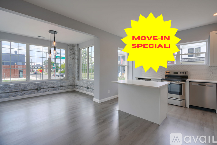 A large, empty room with a kitchen area and a window overlooking the street.