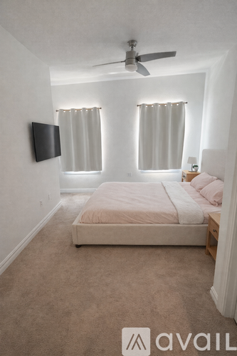 A bedroom with a bed, a ceiling fan, and a flat-screen TV mounted on the wall.