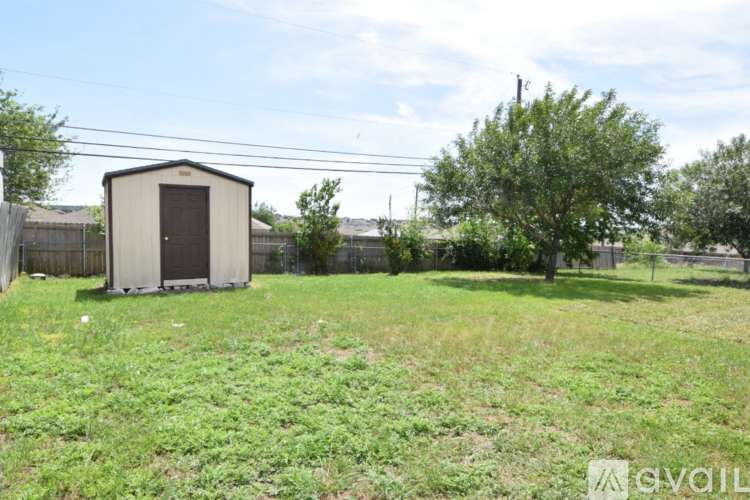 A shed sits in a grassy field with a fence and trees in the background.
