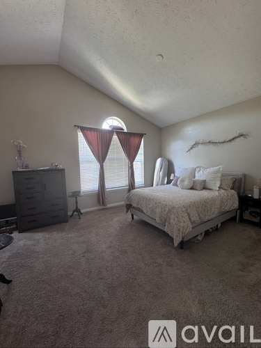 A bedroom with a bed, dresser, and window with curtains.