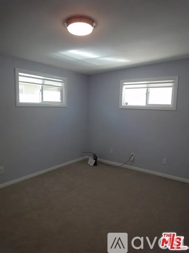 A room with a carpeted floor and two windows.
