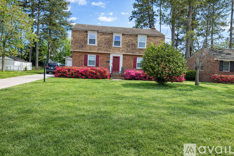A house with a red door and windows is surrounded by green grass and trees.
