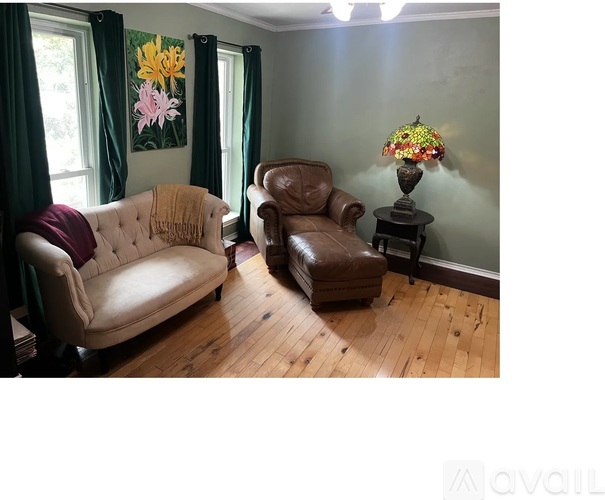 A living room with a beige couch, brown leather chair, and a table with a lamp.