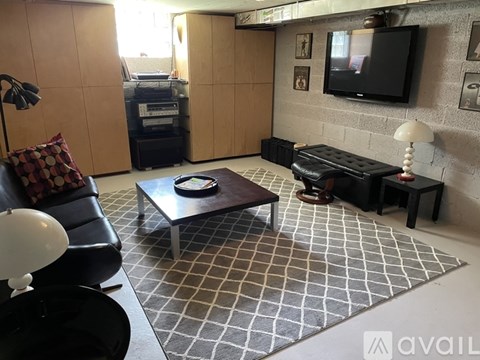 A living room with a black couch, a coffee table, and a television mounted on the wall.