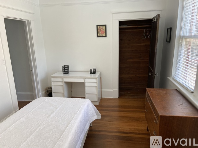 A bedroom with a white bed and a wooden desk.