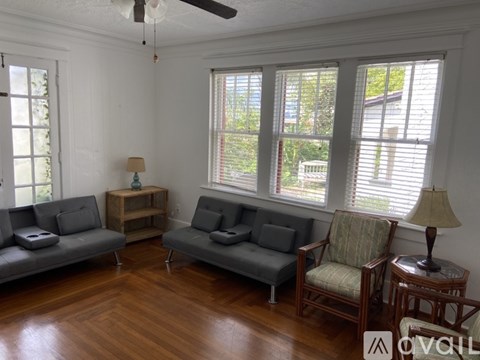 A living room with a grey sofa, a wooden chair, and a wooden side table with a lamp.
