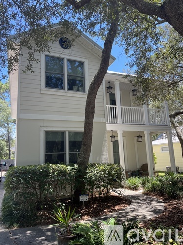 A white house with a balcony and a tree in front.