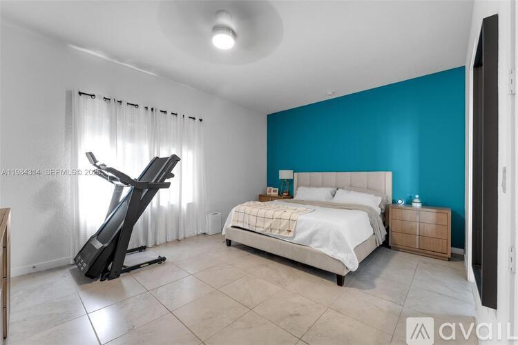 A bedroom with a white bed and a black exercise bike.