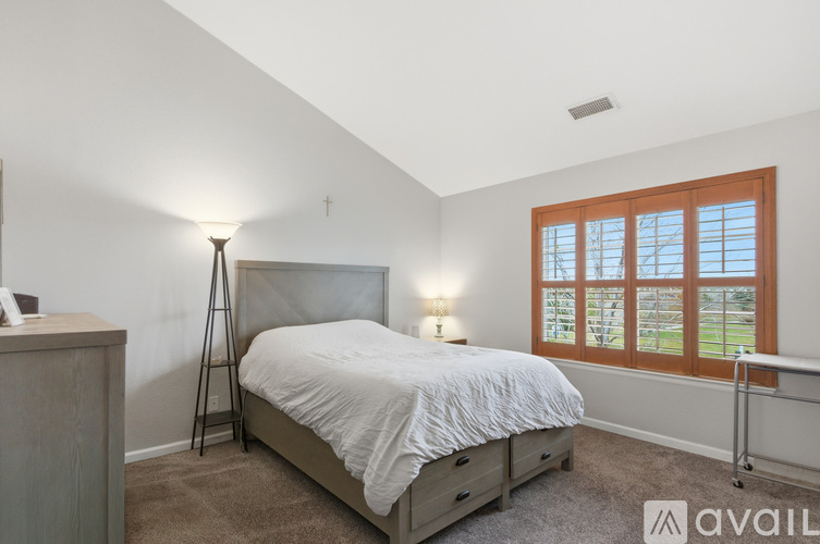 A bedroom with a large bed, a wooden nightstand, and a window with a view of a grassy area.
