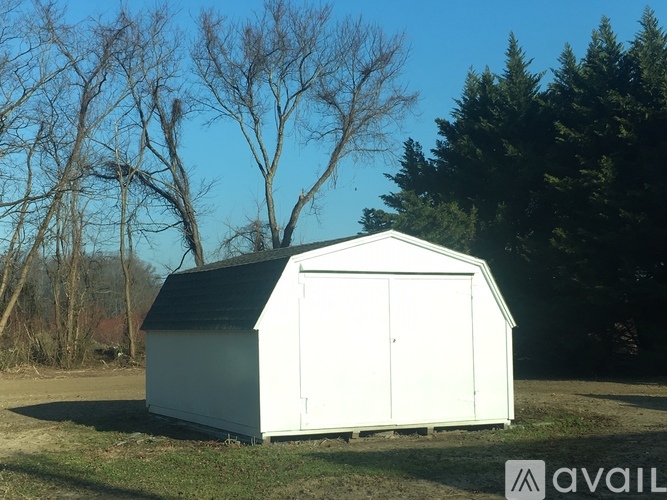 A white shed sits in a field with trees in the background.