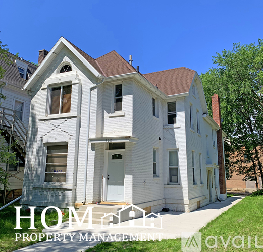 A white two-story house with a brown roof and a sign that says "HOME PROPERTY MANAGEMENT" in front of it.