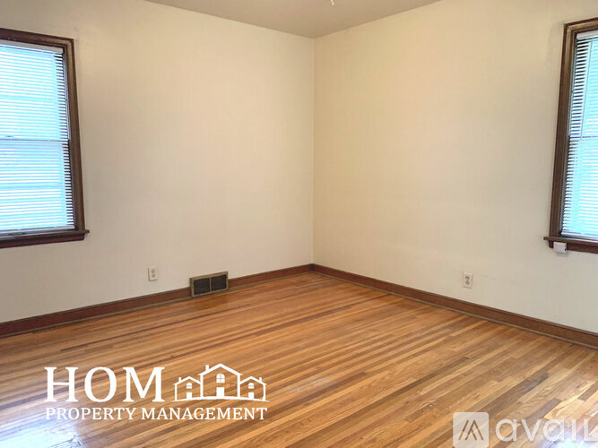 A room with wooden flooring and two windows.