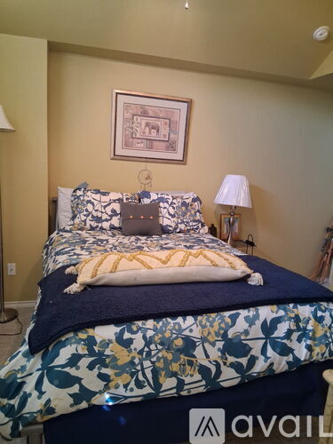A bed with a blue and white comforter and pillows is in a room with a picture on the wall.