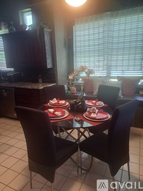 A dining table set with plates and glasses is in the foreground with a kitchen in the background.