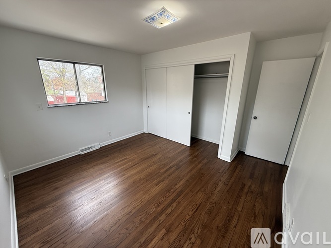 A room with wooden flooring and a window with a view of a tree-lined street.