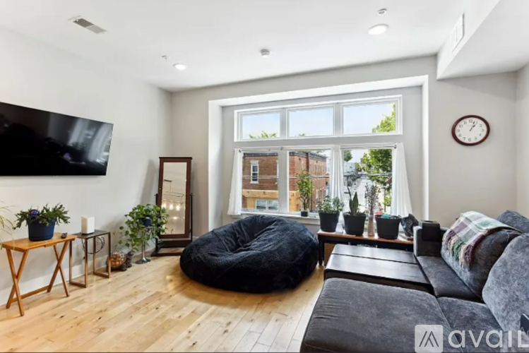 A living room with a large window, a couch, a bean bag chair, and a flat-screen TV mounted on the wall.