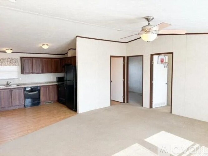 A spacious living room with a kitchen area and a ceiling fan.