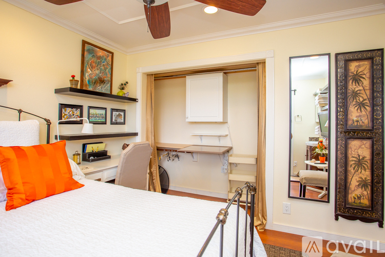 A bedroom with a bed, desk, chair, and a mirror.