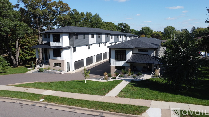 A large white building with a black roof is surrounded by trees and has a grassy front yard.
