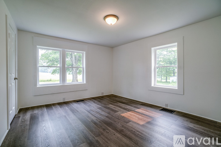 A room with wooden flooring and two windows.