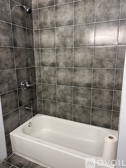 A white bathtub sits in a bathroom with grey tiled walls.