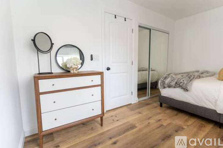 A bedroom with a bed, dresser, mirrors and a door.